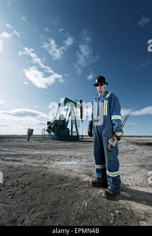 A man in overalls and hard hat at a pump jack in open ground at an oil extraction site. Stock Photo