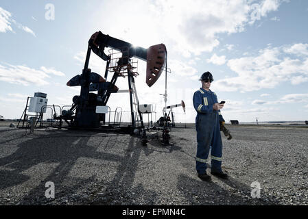 A man in overalls and hard hat at a pump jack in open ground at an oil extraction site. Stock Photo