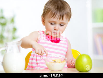 Cute little girl eats healthy food sitting at table in nursery Stock Photo
