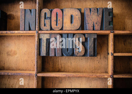 The phrase IN GOD WE TRUST written in vintage wooden letterpress type in a wooden type drawer. Stock Photo