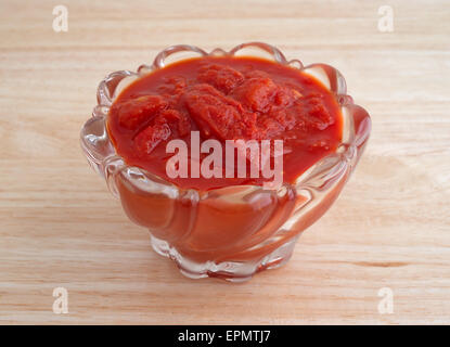 A small bowl filled with crushed tomatoes with jalapeño peppers on a wood table top. Stock Photo