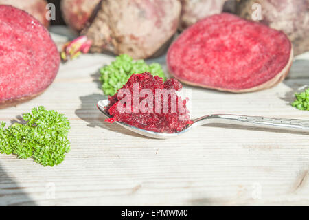 A spoon full of purple beetroot grate, in front of vegetables and herbs Stock Photo