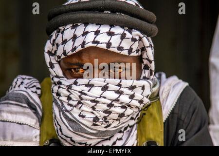 A man dressed up to role play a terrorist looks on as soldiers from Burkina Faso, Senegal and the U.S. Army approach a mock village during a situational training exercise during June 24, 2014 in Thies, Senegal. Stock Photo