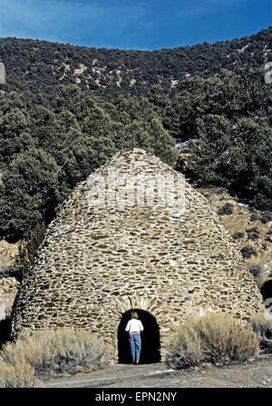 A tourist inspects one of the historic beehive-shaped charcoal kilns built in 1877 to make charcoal for ore smelters used in silver and lead mining operations nearby Death Valley, California, USA. The rock and mortar structures were constructed in Wildrose Canyon in the Panamint Mountains near sources of wood that included pine and juniper trees, which were slowly burned for a week to create the charcoal. The 10 kilns were abandoned when the mines shut down but were restored a century later and have become an attraction in Death Valley National Park. Stock Photo