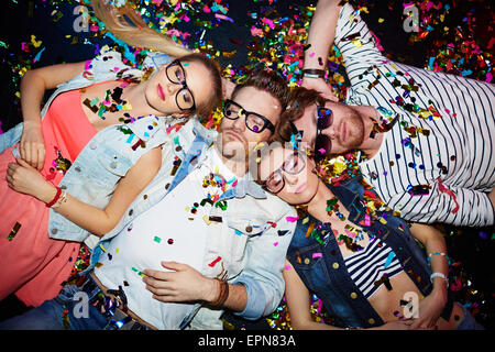 Young friends sleeping in confetti on the floor in nightclub after party Stock Photo