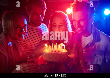 Young girl blowing candles on birthday cake between her friends Stock Photo