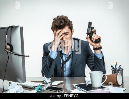 Young businessman with gun wants to commit suicide / modern office man at working place, depression and crisis concept Stock Photo