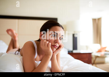 Attractive woman lying in bed resting chin in hands looking sad. Stock Photo