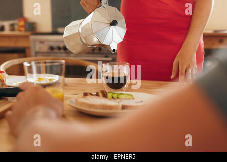 Cropped shot of woman serving black coffee in small glass on breakfast table. Pouring fresh coffee from a jug into a cup. Stock Photo