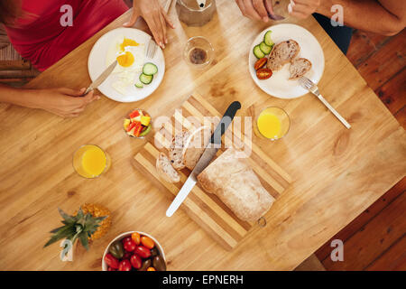 Top view of couple eating a healthy morning breakfast at home. Breakfast table with loaf of bread on cutting board, fruits, juic Stock Photo