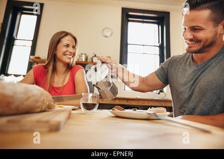 Indoor shot of young man pouring coffee into a cup with his girlfriend having breakfast in kitchen at home. Smiling young couple