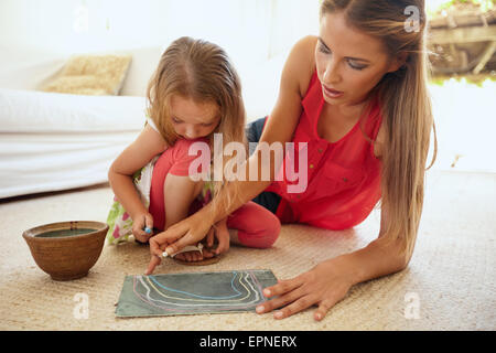 Portrait of mother and little daughter together drawing pictures using color chalks, both sitting on floor in living room at hom Stock Photo