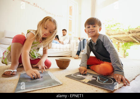 Indoor shot of little children drawing while their father in the background sitting on couch in living room. Stock Photo