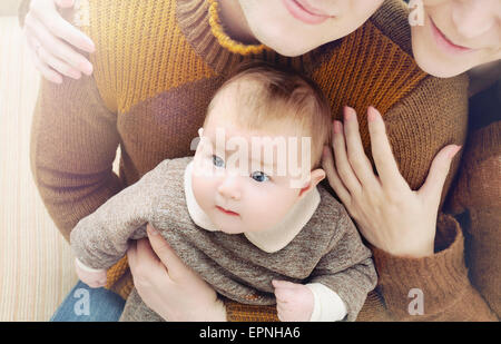 happy family of three, little cute baby with big eyes sitting on the parent's knees, family concept
