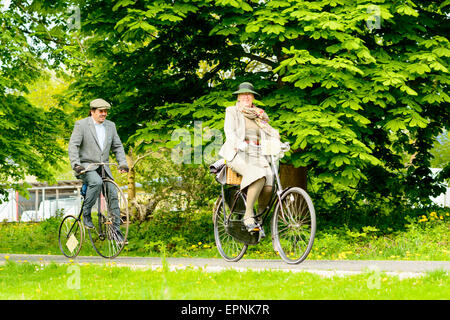 Solvesborg, Sweden - May 16, 2015: International Veteran Cycle Association (IVCA) 35th rally. Costume ride through public streets in town. Man on small penny-farthing and woman on bike. Stock Photo