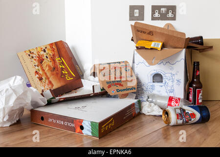 Fast food litter. Discarded drinks cans, bottles and takeaway pizza boxes on the floor at the edge of a room, UK Stock Photo