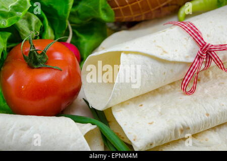Empty tortillas tied with a red ribbon on a table with tomato, lettuce and ham Stock Photo