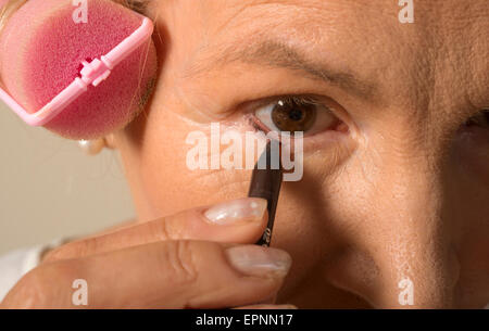 Woman in curlers applying eyeliner Stock Photo