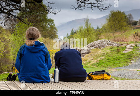 Two hikers picnicking on bridge spanning the Upper Falls of Aira Beck, above Aria Force, near Ullswater, Lake District, Cumbria Stock Photo
