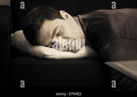 Man lying and resting on sofa at home. He is sleeping with his head on a pillow. Stock Photo