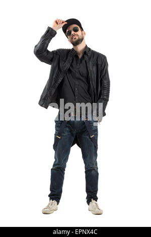 Young bearded man holding cap wearing sunglasses looking at camera. Full body length portrait isolated over white background. Stock Photo