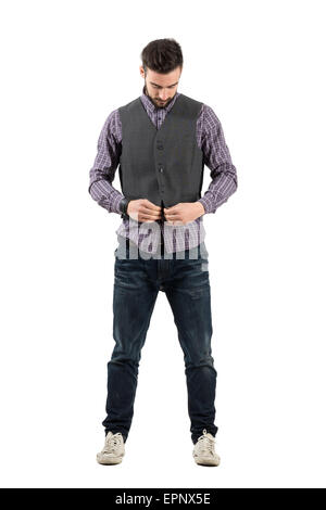 Young bearded man buttoning waistcoat looking down. Full body length portrait isolated over white background. Stock Photo