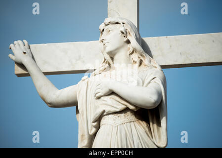 Granada Municipal Cemetery White Marble Woman Cross Statue Granada Nicaragua | GRANADA, Nicaragua — A white marble figure of a mourning woman clasps a cross in close detail at the Cementerio de Granada, an example of the neoclassical funerary statuary that fills Nicaragua's oldest municipal cemetery. Much of this Carrara-marble sculpture was imported from Italy and commissioned by Granada's Conservative-era merchant elite through the late nineteenth century. Stock Photo