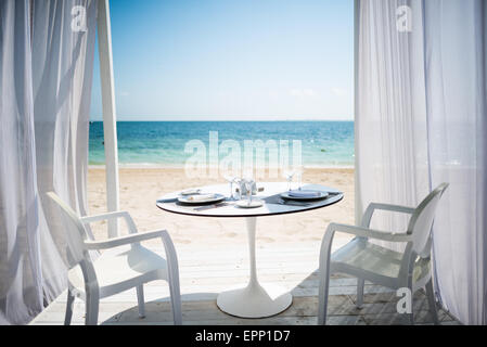 Romantic Beach Dinner Playa Mujeres Mexico | PLAYA MUJERES, Mexico — A table set for two waits beneath sheer curtains on the sand at the Beloved Hotel in Playa Mujeres, staged ahead of a private beachfront dinner overlooking the Caribbean Sea north of Cancun. Oceanfront dining setups like this are a signature offering of luxury resorts along Mexico's Costa Mujeres corridor, aimed at couples and honeymooners. Stock Photo