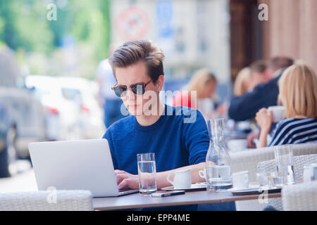 Young Man with Laptop Sitting in Outside Coffeehouse Working Stock Photo