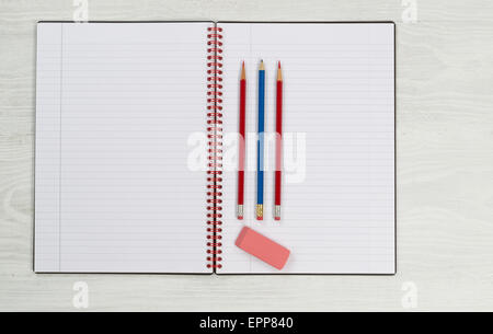 Blank new notepad, in open position, with sharpen pencils and eraser on rustic white desktop. Stock Photo