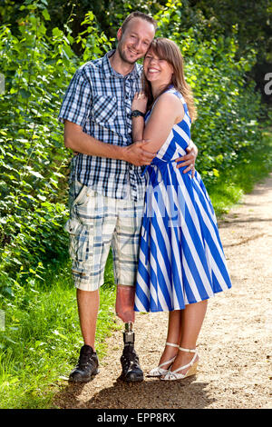 Confident attractive smiling young couple in a loving embrace standing outdoors on a gravel path - the man with prosthetic leg. Stock Photo