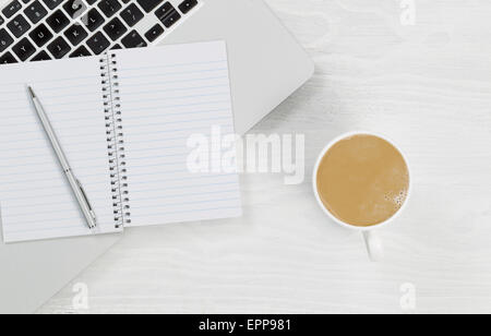 High angle view of laptop, coffee and blank notepad with silver pen on rustic white desktop. Stock Photo
