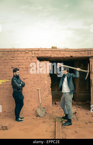Guy pulling down a wall while another one is watching Stock Photo