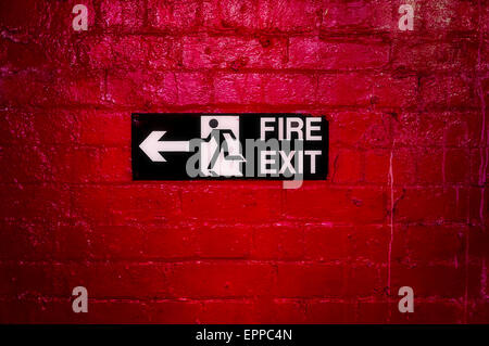 Sign Informing about the fire escape hung on a brick wall painted red. Stock Photo