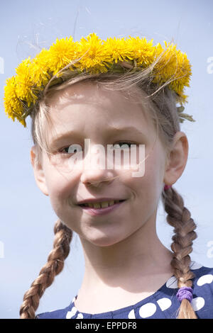 young girl portrait in yellow dandelion garland on blue sky background Stock Photo