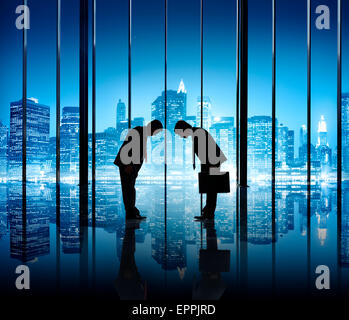 Two businessmen bowing to each other in an office building. Stock Photo