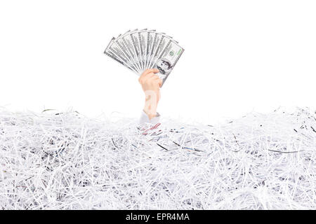 Studio shot of a hand of a man stuck in a pile of shredded paper holding a stack of money above the surface Stock Photo