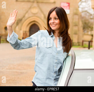 young woman leaning out of car window waving. Stock Photo