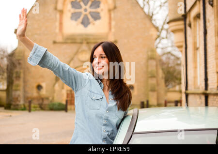 young woman waving out of car window Stock Photo