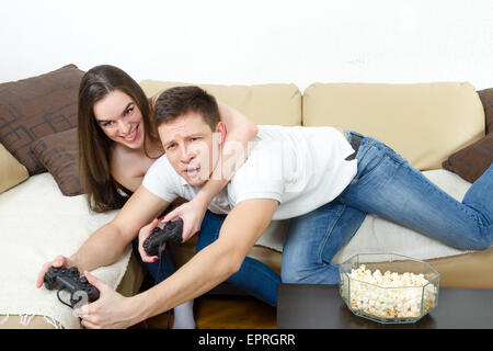Young couple sitting in living room and play video games on console or pc with joysticks while looking in screen or TV. Lifestyl Stock Photo