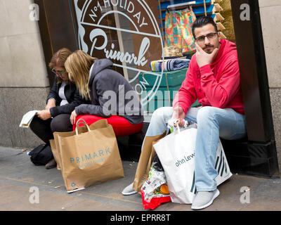Shoppers resting outside after buying at Primark, Oxford Street, London Stock Photo
