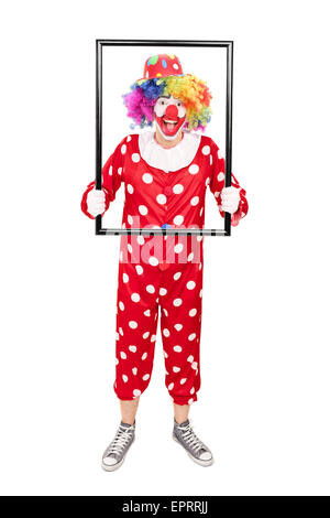 Full length portrait of a male clown holding a big picture frame and posing behind it isolated on white background Stock Photo