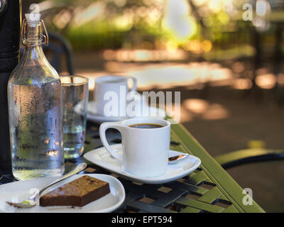 Coffee in white cups and saucers, water bottle and glass with chocolate brownie on plate at outdoor patio, Canada Stock Photo