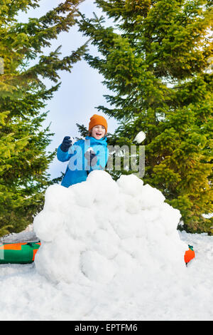 Laughing boy in blue winter jacket plays snowballs Stock Photo