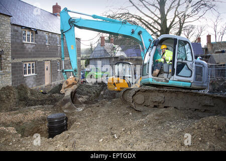 A construction worker uses an excavator to install the drainage system on a small, rural housing development in Dorset, UK Stock Photo