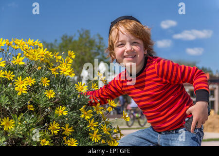 boy sitting next to flowers yellow daisies Stock Photo