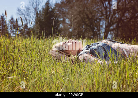 Young woman laying in tall grass looking up to sky in deep thought Stock Photo