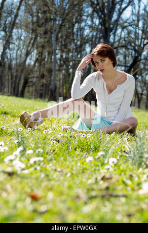 Beautiful woman sitting in the grass surrounded by spring daisies Stock Photo
