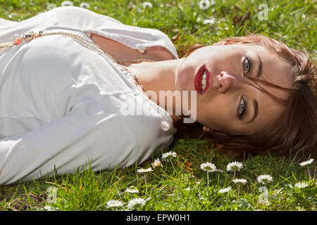 Beautiful woman laying in the grass surrounded by spring daisies Stock Photo