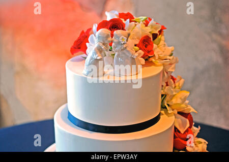 white cherubs top a white wedding cake decorated with red roses and jasmine Stock Photo